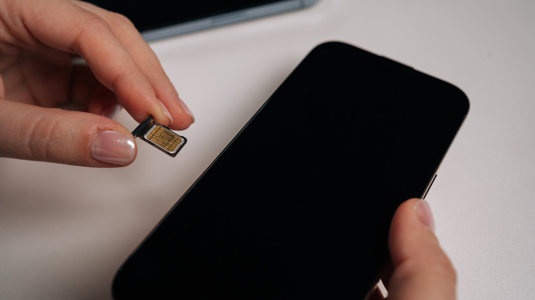 Someone inserting a physical SIM card into the tray and inserting the tray into the smartphone.