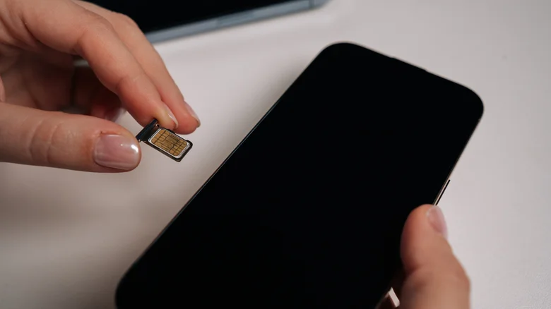Someone inserting a physical SIM card into the tray and inserting the tray into the smartphone.