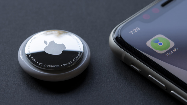 An Apple AirTag on a table beside an iPhone showing the Find My app.