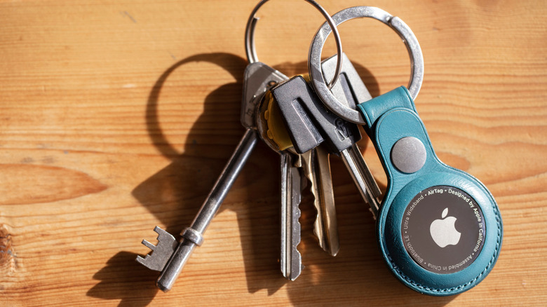 A set of keys on a table with an Apple AirTag attached to them via keyring holder.