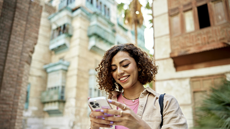 A woman smiles while holding her smartphone.