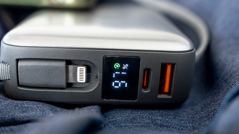 A portable power bank with a digital display, Lighting connector, orange USB-C port and an orange USB-A port.