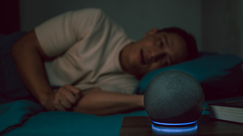 A man lying in bed next to a glowing Amazon Echo Dot.