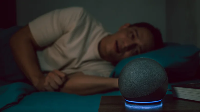 A man lying in bed next to a glowing Amazon Echo Dot.