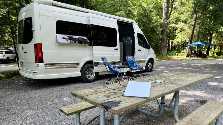 A Starlink Mini dish on a wooden table, with a campervan parked nearby.