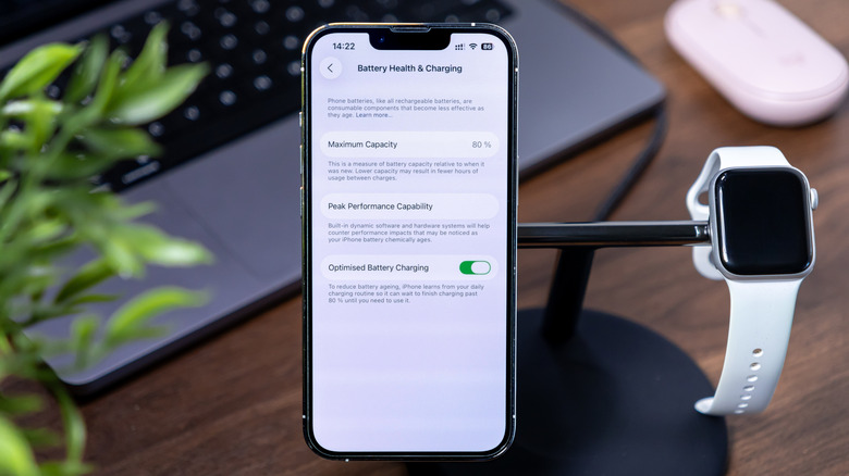 An iPhone on a stand with an Apple Watch, with its screen displaying the battery health menu.