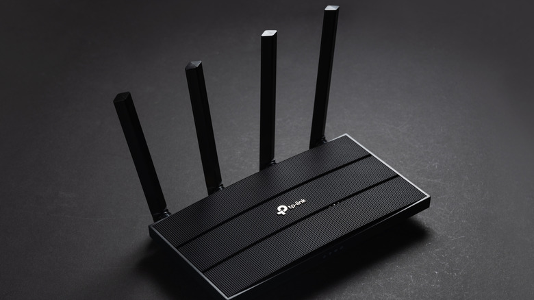 A black TP-Link router sits upon a black table.