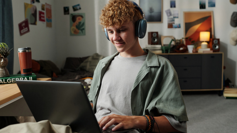 Boy wearing headphones, smiling while looking at a laptop in his lap.