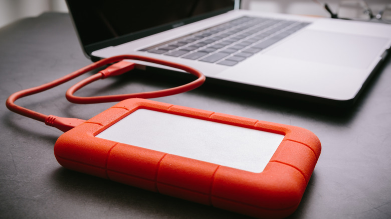 An external hard drive in an orange storage case, connected to a laptop.
