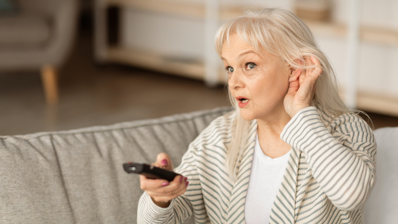 A woman struggles to hear while watching TV.