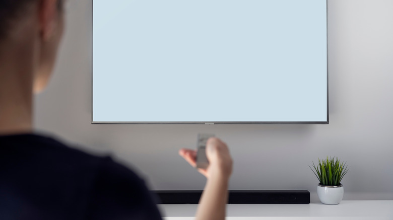A man holding his TV remote toward his TV and soundbar.