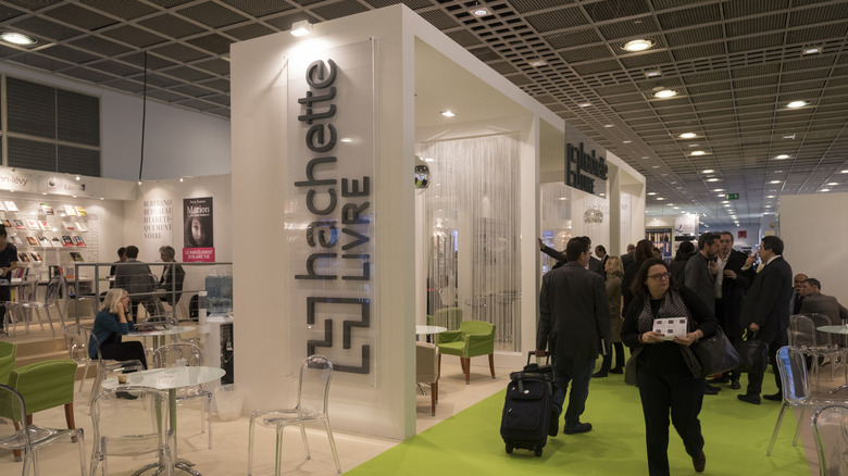 Photo of the Hachette booth at the 2025 Frankfurt Book Fair. White shelves mark the space around a lime green walkway. Lucite and lime green chairs and tables are on the left near displays of books.