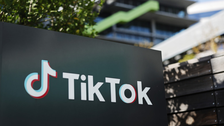 The TikTok logo on a sign with an office building in the background.