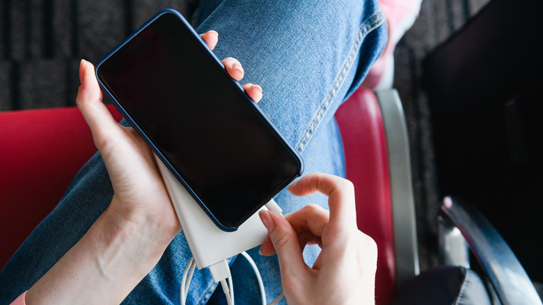 The legs of a woman on a flight with her phone plugged into a portable power bank.