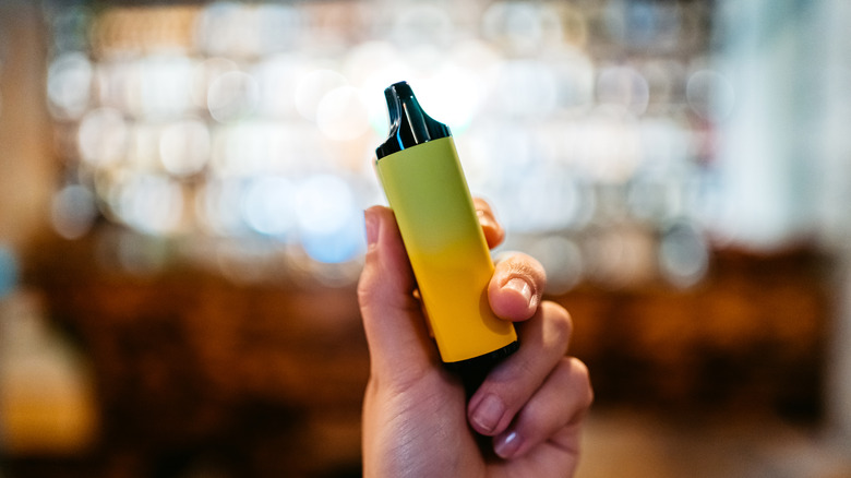 A woman holding up a yellow vape.