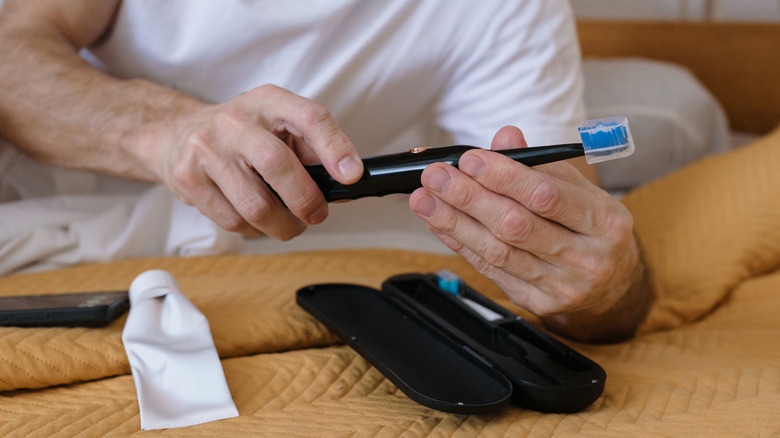 A man's hands holding an electric toothbrush above its storage case.