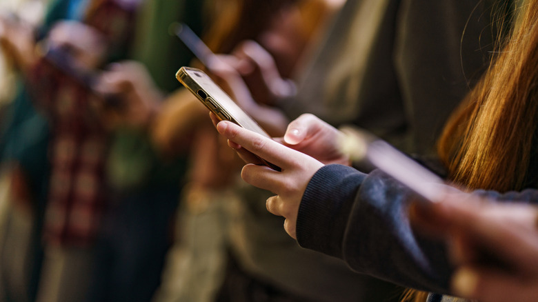 A smartphone shown in a young person's hand with other young people using smartphones in the background