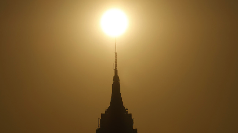 Photo of the sun behind the spire of the Empire State Building. Wildfire smoke has given the sky a sickly, yellowed cast.