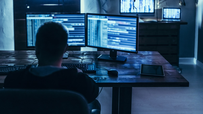 A person sitting in front of multiple computer monitors in a dark room.