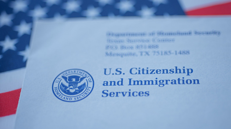 Close-up of an envelope with the return address of the US Citizenship and Immigration Services department seen above an out-of-focus American flag.
