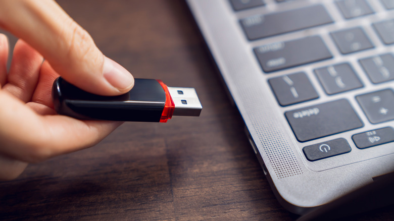A hand about to plug a USB drive into a laptop.