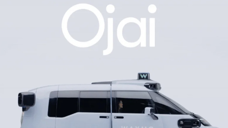 Promotional image of the upper half of the passenger side of a pale blue Waymo Ojai driverless van. The word 