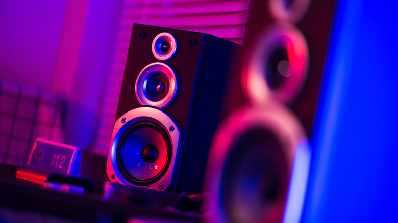 A pair of bookshelf speakers on a table, bathed in purple light.