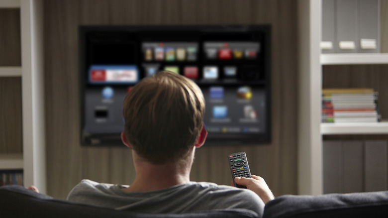 A man holding a TV remote, pointing it towards a smart TV.