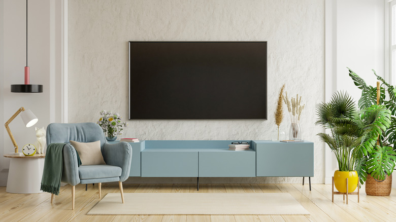 A wall-mounted TV situated in a modern living room with chairs and plants.