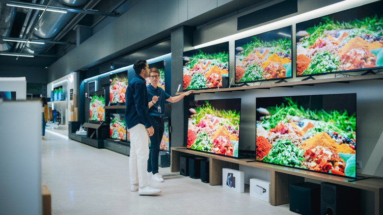 A man viewing smart TVs on sale in a retail store as an employee explains them.