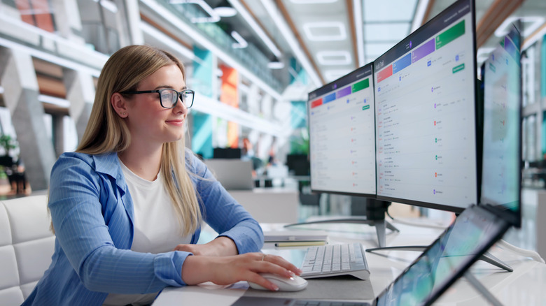 A woman smiling at her desk while using two monitors.