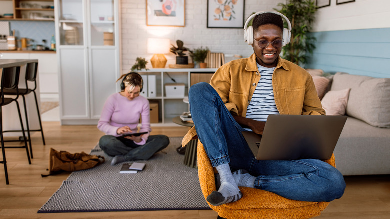 A man using wireless headphones with a laptop, with a woman using a tablet behind him.
