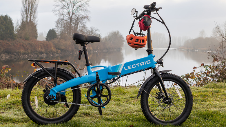 A folding electric Lectric e-bike, unfolded next to a lake with a rider's helmet.