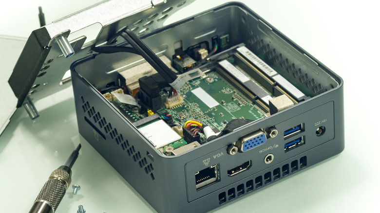 A mini PC with the top cover removed, with screwdriver and screws visible.