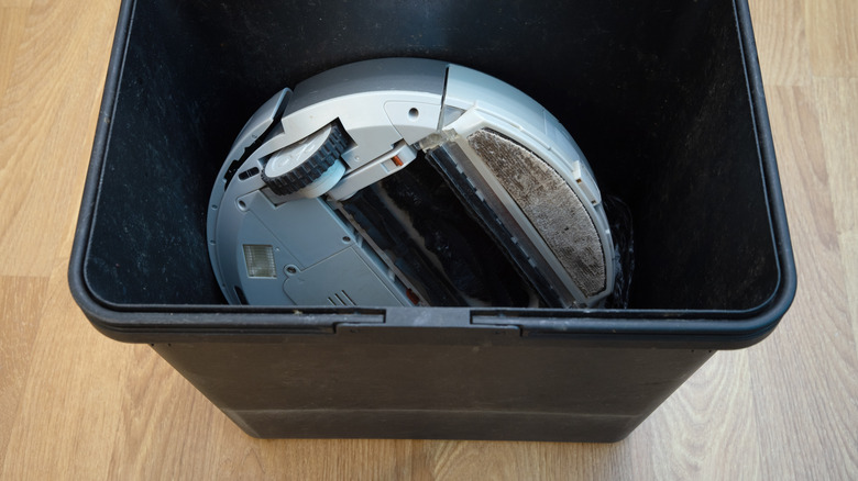 A broken robot vacuum cleaner, placed in a trash can.