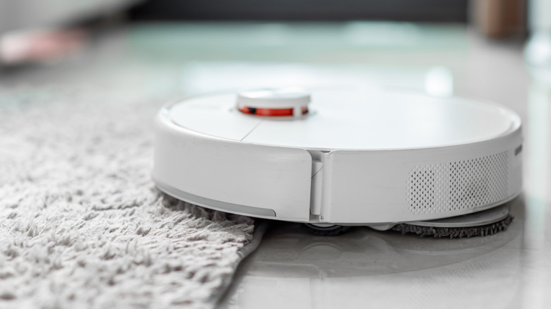 A close up of a robot vacuum cleaner moving from tiled floor to carpet.