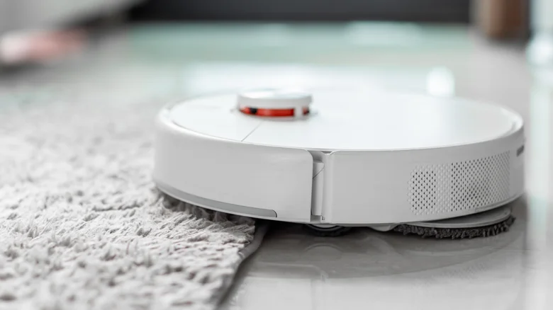 A close up of a robot vacuum cleaner moving from tiled floor to carpet.