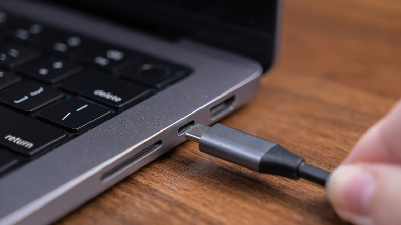 A hand plugs a USB-C cable into a USB-C port on a MacBook.