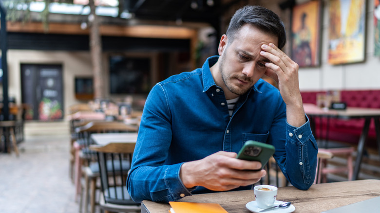 A man looking upset while looking at his iPhone in a cafe.