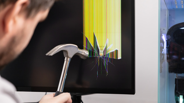 A person hitting a broken monitor with a hammer.