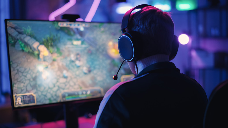 Person wearing headphones playing PC games in a dark room in front of a computer monitor.
