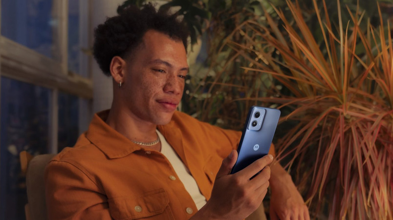 A person sitting and looking at their Moto G Play (2024) smartphone.