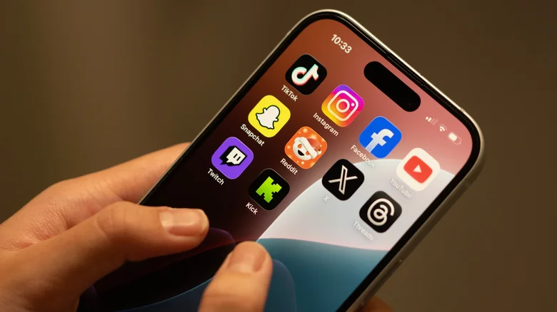 Hands holding an iPhone with various social media app icons on the home screen.