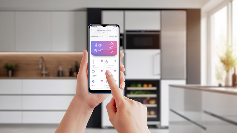 In a kitchen, a person's hands hold up a phone with a smart fridge app open.