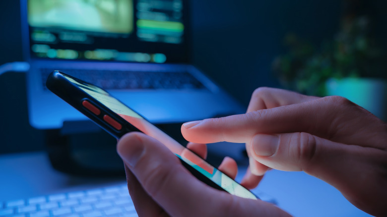 An unknown person uses a phone in front of their laptop