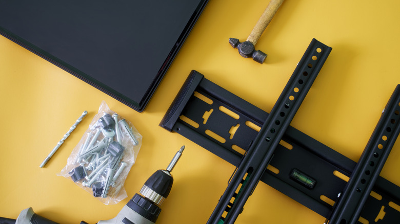 TV wall-mounting hardware and tools laid out beside a flat-screen TV on a yellow surface.
