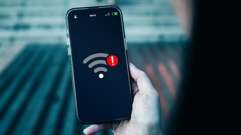 A person holding a phone showing a Wi-Fi connection with a red warning sign above it.