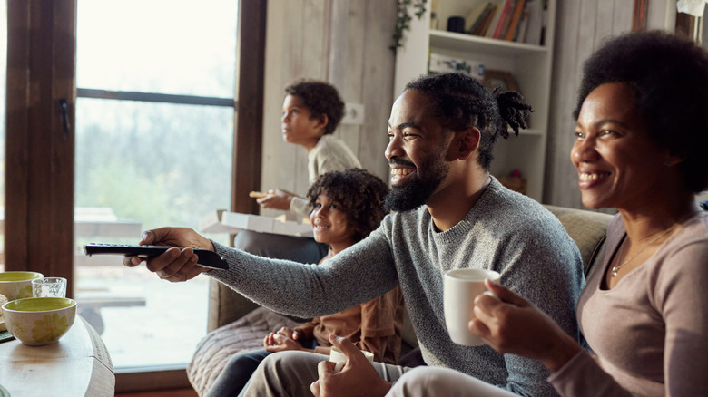 A family smiles as they change the channel on their television set.