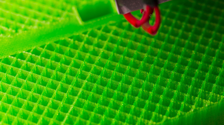 Close-up of a 3D printer building a green lattice infill structure.