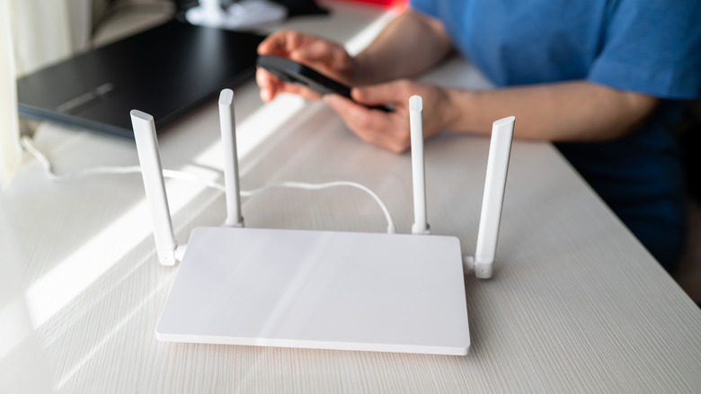A white Wi-Fi router with protruding antennas, connecting a nearby laptop and smartphone.